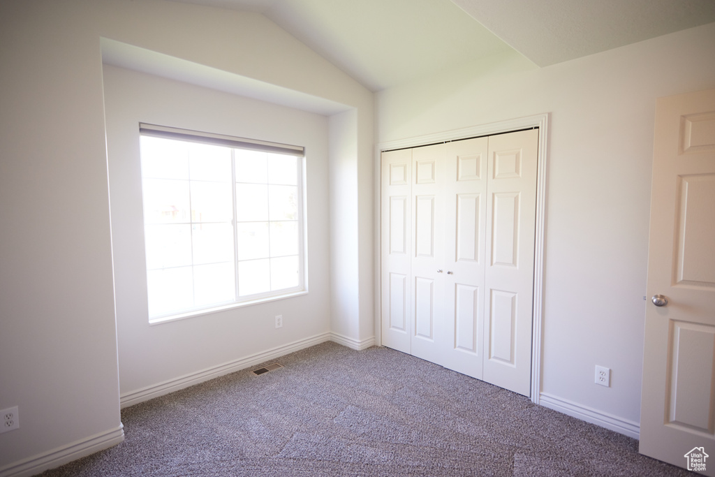 Unfurnished bedroom with carpet, a closet, and lofted ceiling