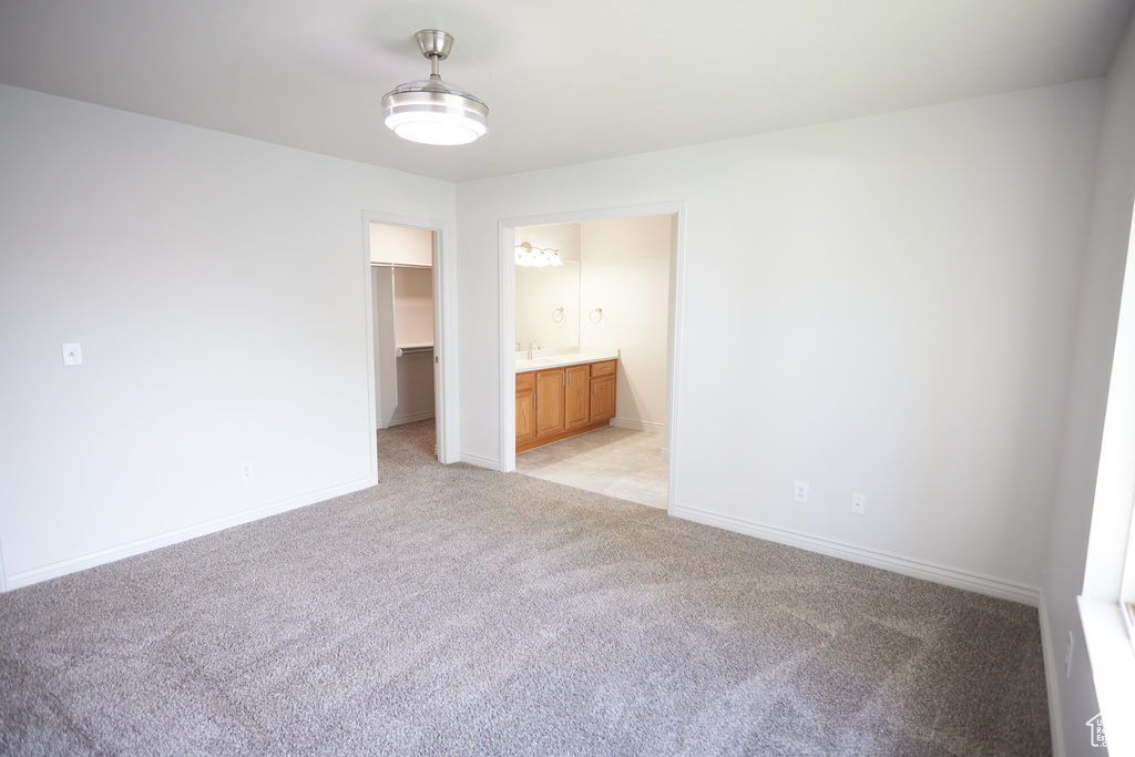 Unfurnished bedroom featuring light colored carpet, a closet, a walk in closet, and ensuite bathroom