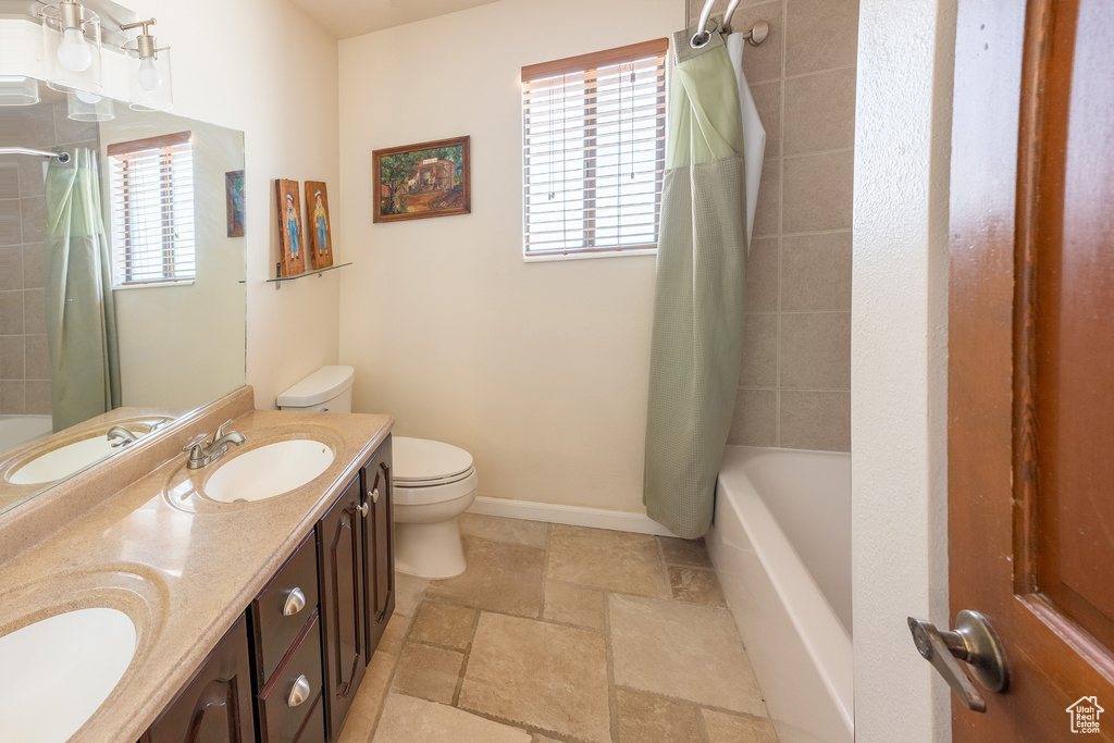 Full bathroom with dual bowl vanity, shower / bath combination with curtain, tile floors, and toilet