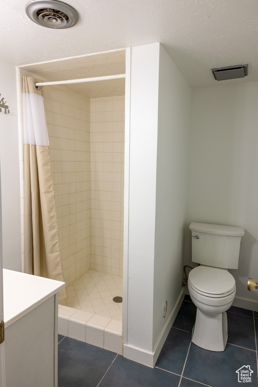 Bathroom featuring toilet, a shower with curtain, a textured ceiling, vanity, and tile floors
