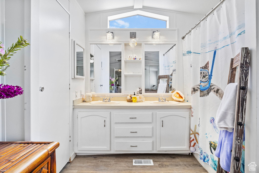 Bathroom featuring hardwood / wood-style floors, lofted ceiling, oversized vanity, and dual sinks