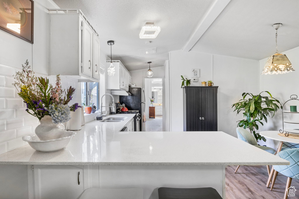 Kitchen with vaulted ceiling, kitchen peninsula, white cabinetry, and a kitchen breakfast bar