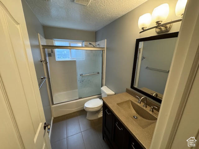 Full bathroom featuring toilet, tile flooring, a textured ceiling, vanity, and shower / bath combination with glass door