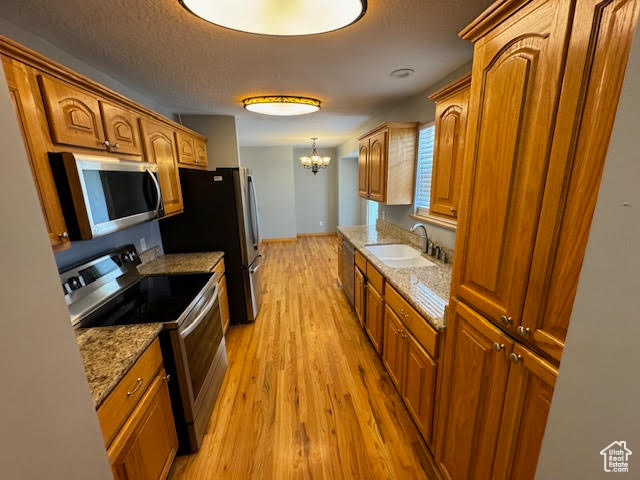 Kitchen with pendant lighting, light hardwood / wood-style flooring, appliances with stainless steel finishes, sink, and light stone counters