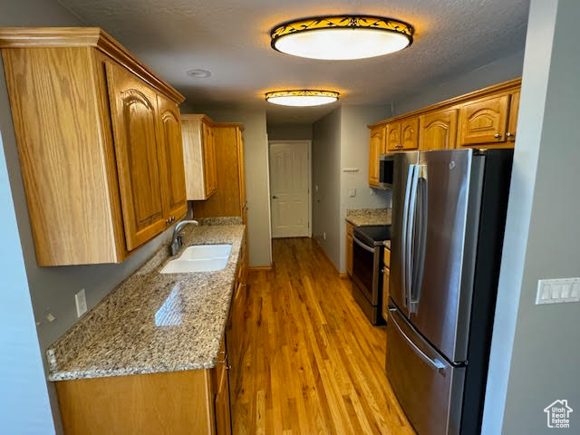 Kitchen featuring sink, light hardwood / wood-style flooring, stainless steel appliances, and light stone counters