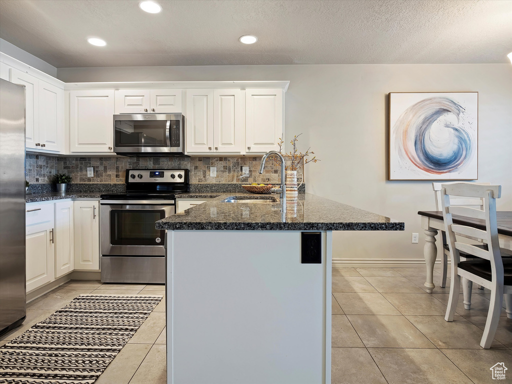 Kitchen featuring backsplash, stainless steel appliances, light tile flooring, dark stone counters, and sink
