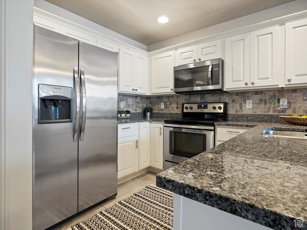 Kitchen featuring appliances with stainless steel finishes, backsplash, white cabinetry, and dark stone counters