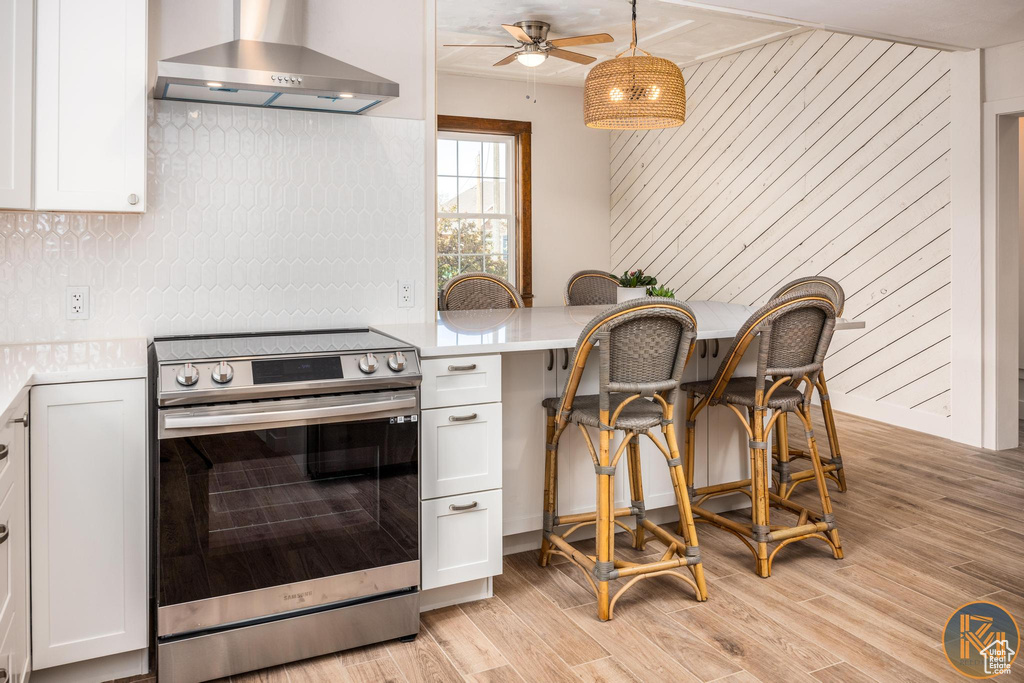 Kitchen featuring wall chimney range hood, electric range, white cabinetry, and light hardwood / wood-style floors