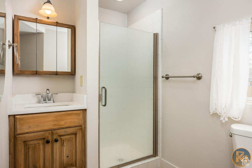 Bathroom featuring a shower with shower door, toilet, and oversized vanity