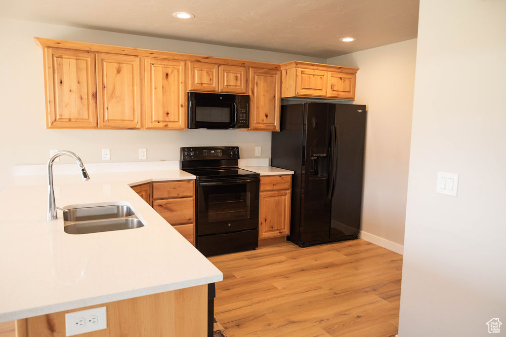Kitchen with sink, kitchen peninsula, light hardwood / wood-style floors, and black appliances