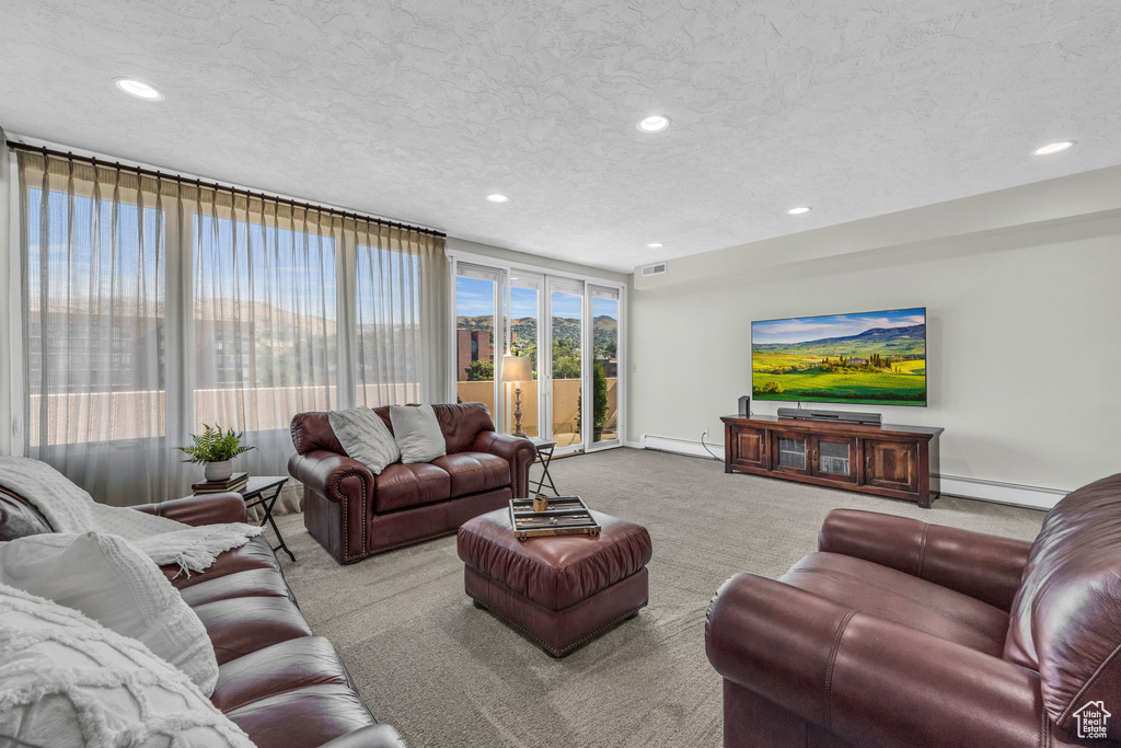 Carpeted living room featuring floor to ceiling windows, a baseboard radiator, and a textured ceiling