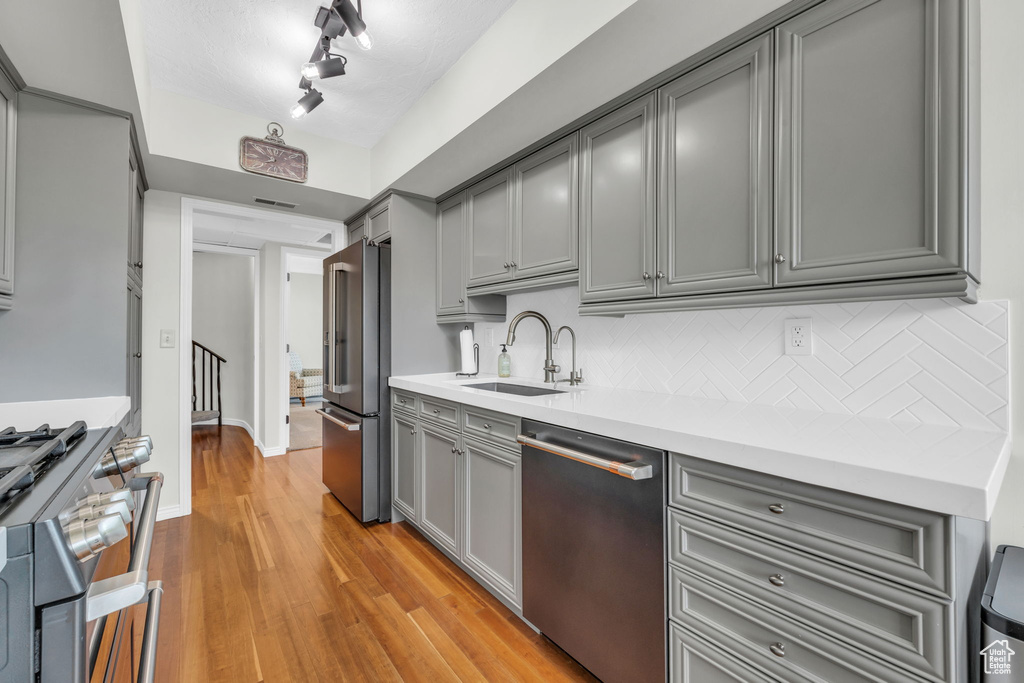 Kitchen with appliances with stainless steel finishes, gray cabinets, light hardwood / wood-style floors, track lighting, and sink