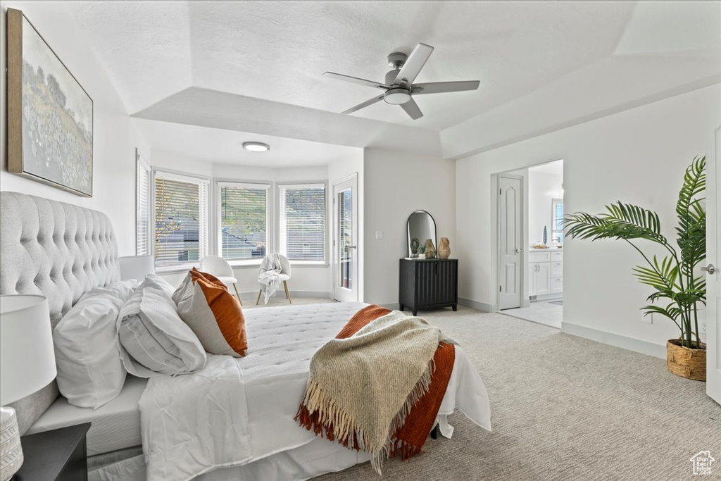 Carpeted bedroom featuring ceiling fan, a raised ceiling, and ensuite bathroom
