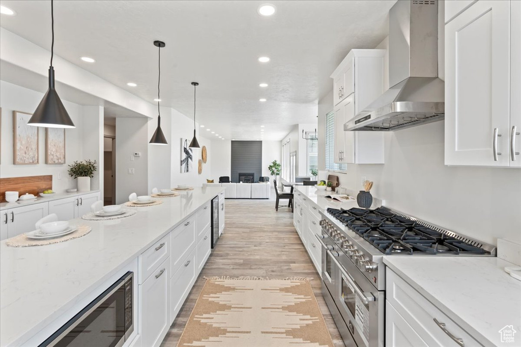 Kitchen with light stone countertops, appliances with stainless steel finishes, light hardwood / wood-style floors, wall chimney exhaust hood, and white cabinetry
