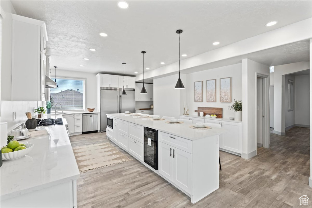 Kitchen with a kitchen island, light hardwood / wood-style flooring, hanging light fixtures, beverage cooler, and white cabinetry