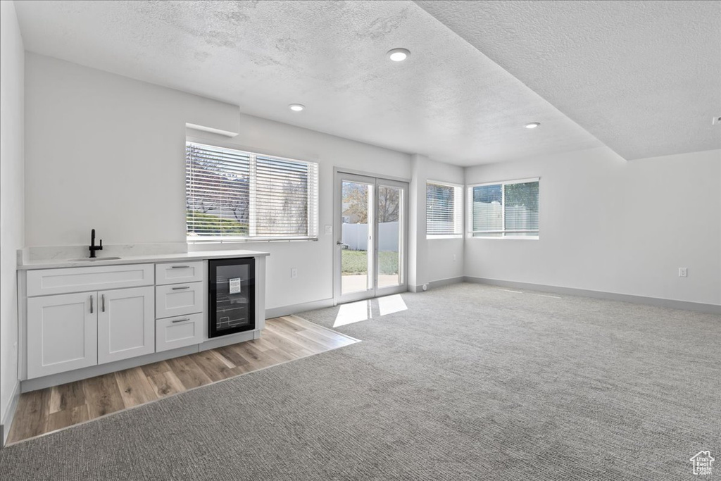 Interior space featuring white cabinets, a textured ceiling, light carpet, and beverage cooler