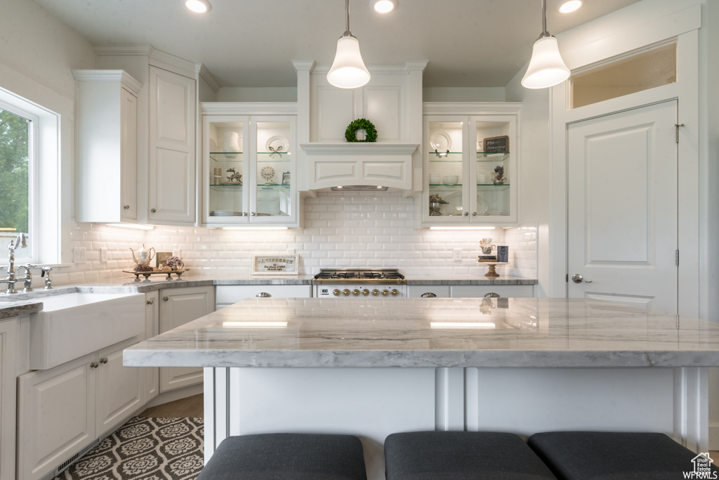Kitchen with light stone countertops, tasteful backsplash, white cabinetry, pendant lighting, and a center island
