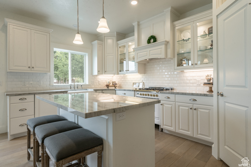 Kitchen with white cabinets, light hardwood / wood-style flooring, tasteful backsplash, and a kitchen island