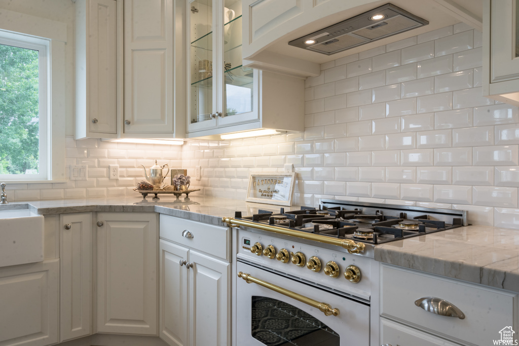 Kitchen with white cabinets, tasteful backsplash, high end range, and light stone counters