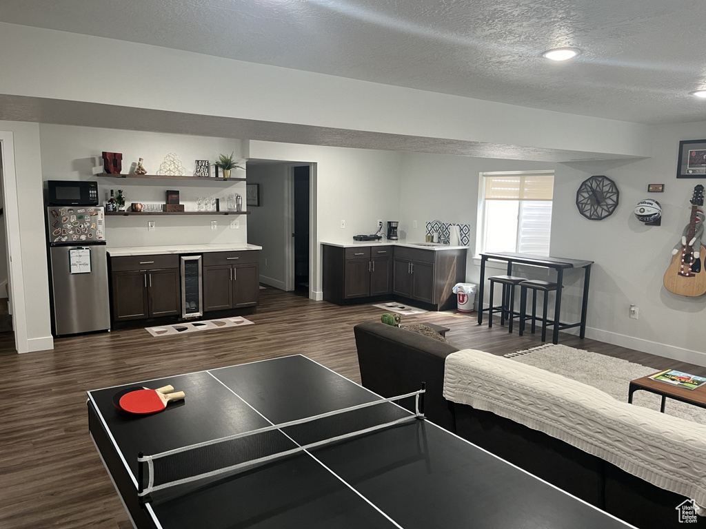 Recreation room featuring a textured ceiling, dark hardwood / wood-style flooring, and beverage cooler