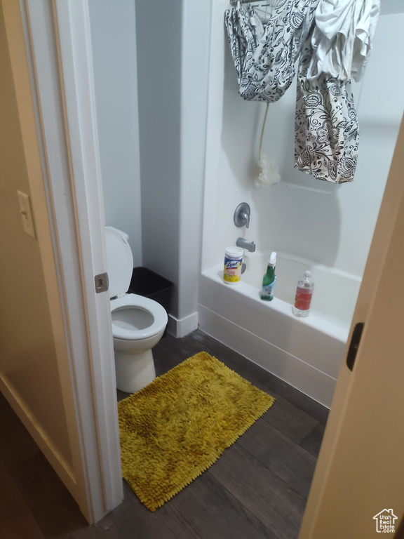 Bathroom with hardwood / wood-style floors, washtub / shower combination, and toilet
