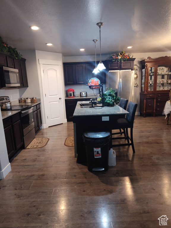 Kitchen featuring hanging light fixtures, dark hardwood / wood-style floors, stainless steel appliances, sink, and an island with sink