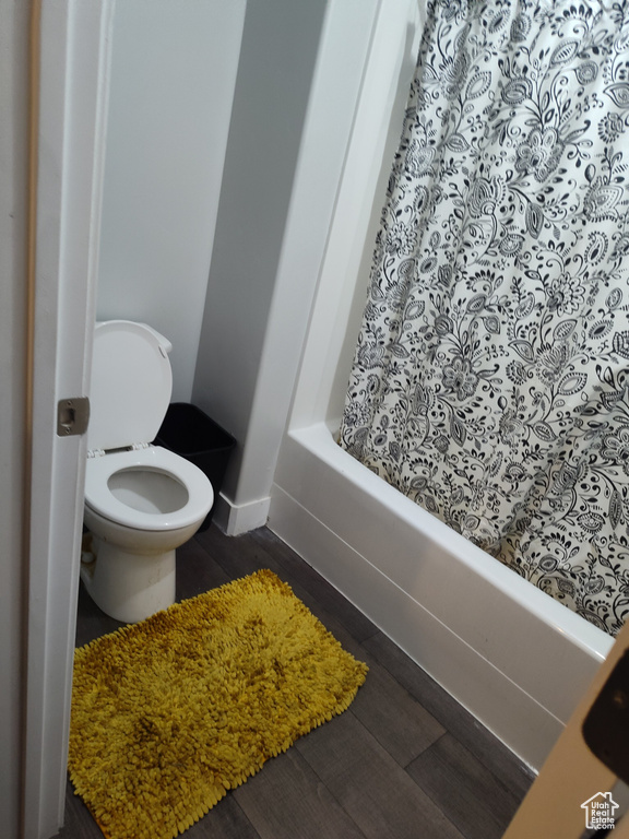 Bathroom with shower / tub combo with curtain, hardwood / wood-style floors, and toilet