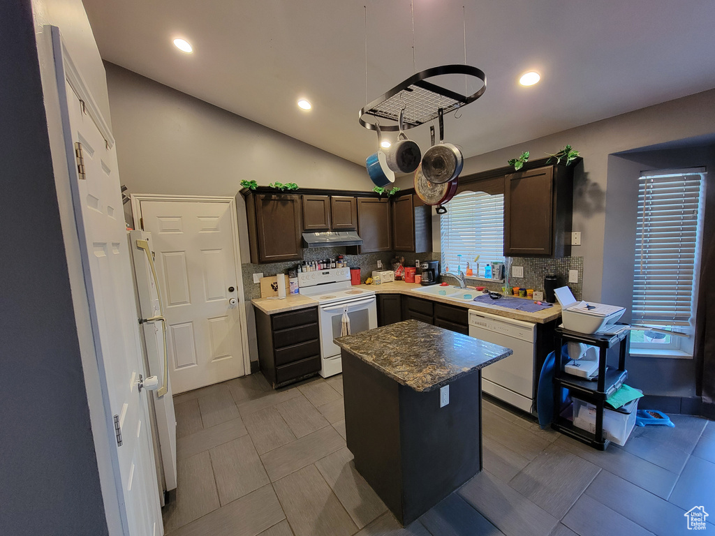 Kitchen with dark brown cabinetry, a kitchen island, white appliances, backsplash, and vaulted ceiling
