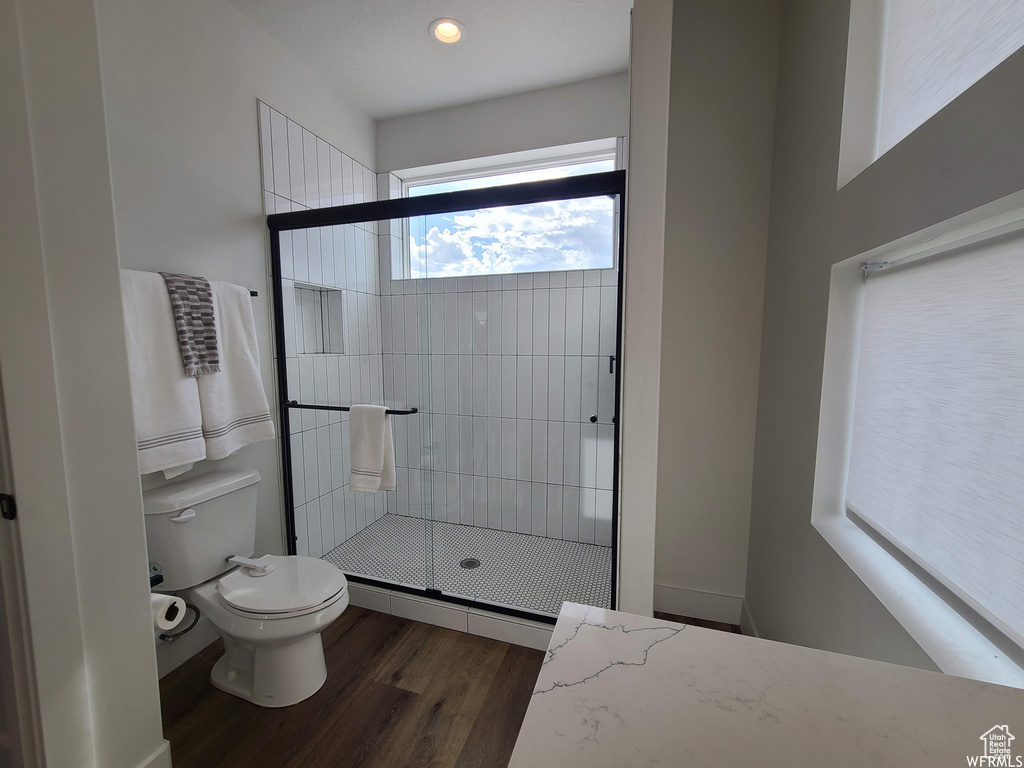 Bathroom with hardwood / wood-style floors, toilet, and a shower with shower door