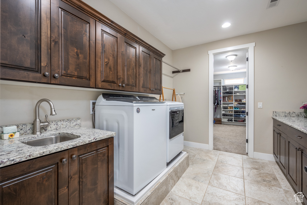 Laundry room with sink, washing machine and dryer, light tile floors, and cabinets