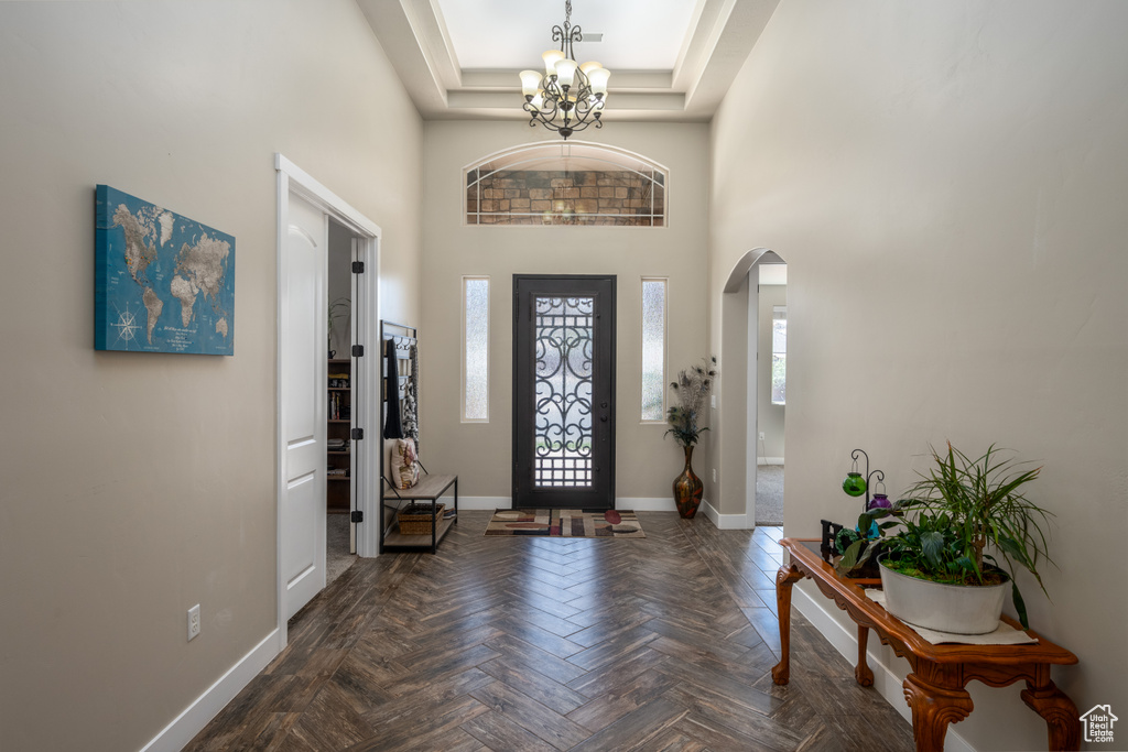 Foyer entrance featuring a chandelier, a towering ceiling, dark parquet floors, and a tray ceiling