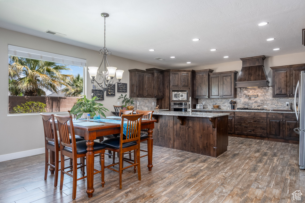 Kitchen with premium range hood, backsplash, appliances with stainless steel finishes, hanging light fixtures, and dark wood-type flooring