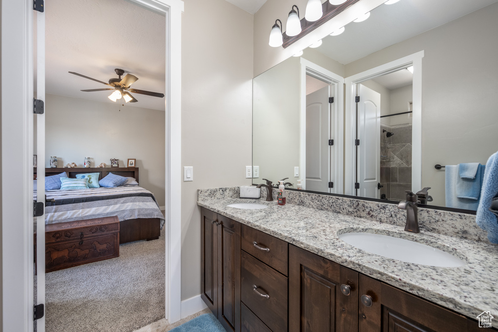 Bathroom featuring tiled shower, ceiling fan, double sink, and large vanity