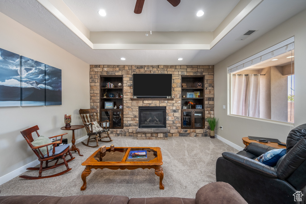 Living room featuring a fireplace, a raised ceiling, ceiling fan, and carpet floors