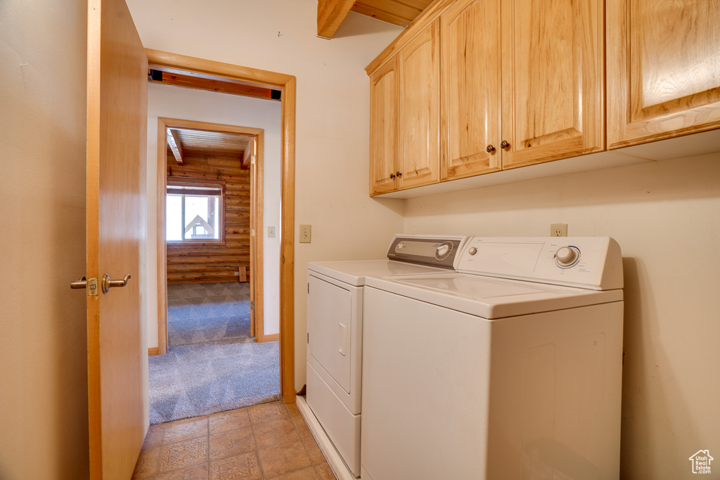 Clothes washing area featuring cabinets, light tile floors, washer and dryer, and log walls