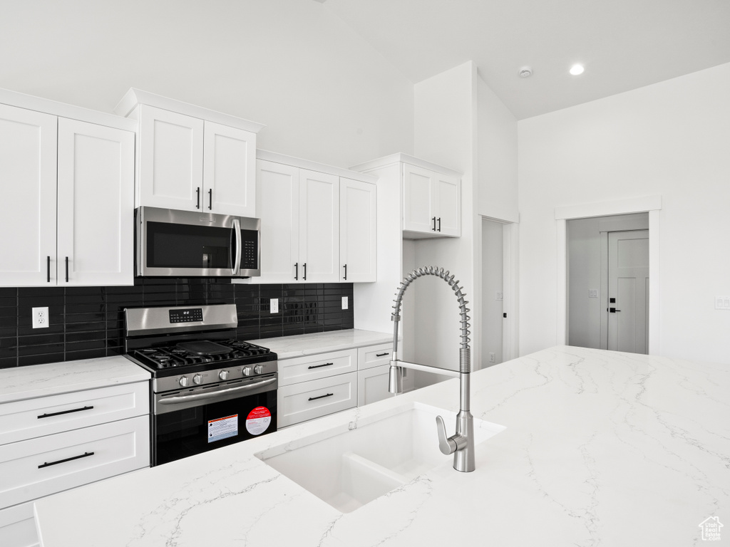 Kitchen with white cabinets, sink, stainless steel appliances, and light stone counters