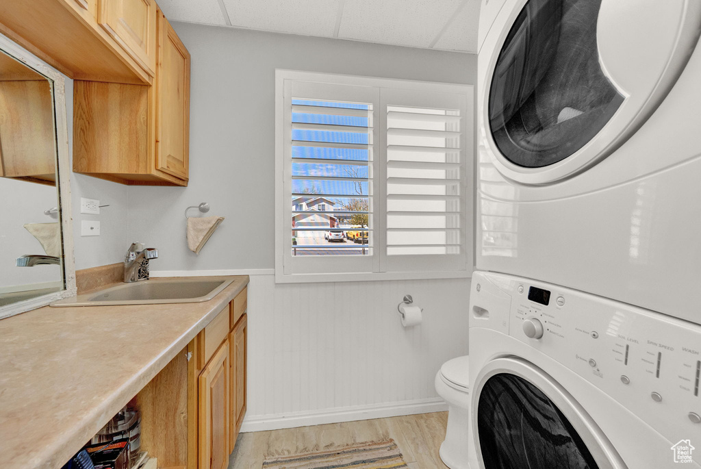 Laundry area featuring sink, stacked washer and clothes dryer, and light wood-type flooring