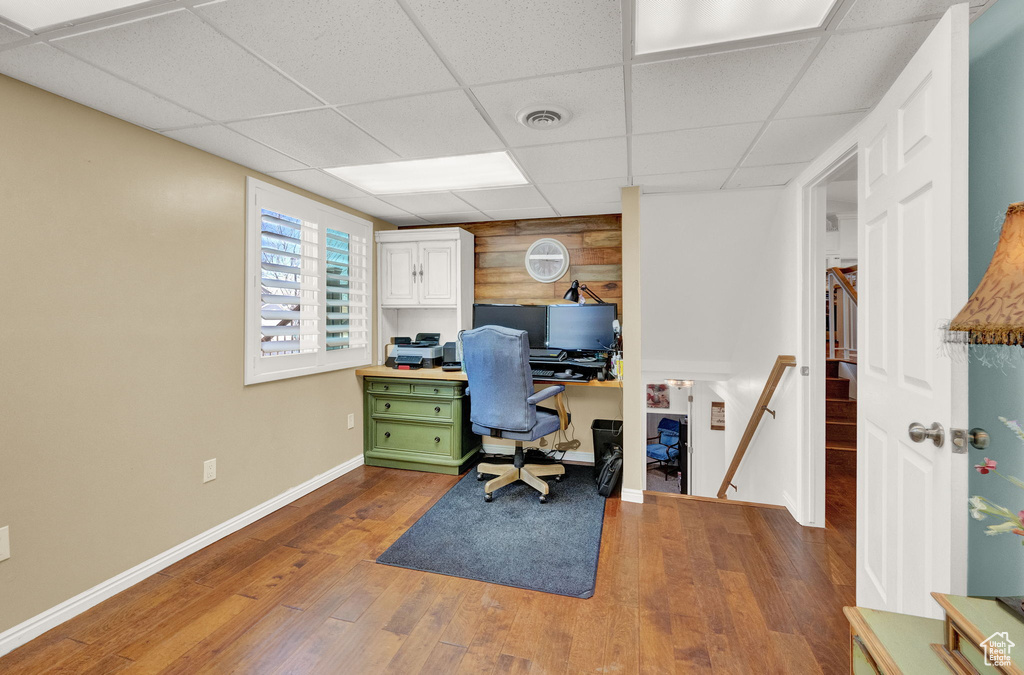 Office space featuring a drop ceiling, hardwood / wood-style flooring, and wooden walls