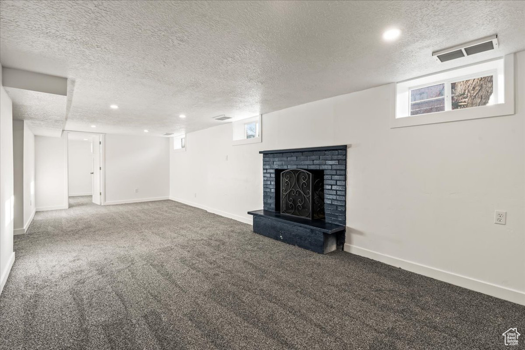 Unfurnished living room with a textured ceiling, carpet, and a brick fireplace