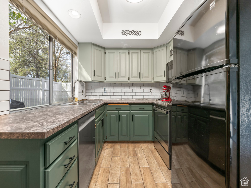 Kitchen featuring light hardwood / wood-style flooring, tasteful backsplash, sink, a raised ceiling, and stainless steel dishwasher