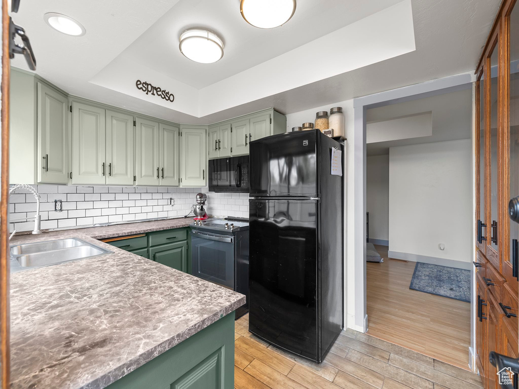 Kitchen with backsplash, light hardwood / wood-style floors, black appliances, sink, and a raised ceiling