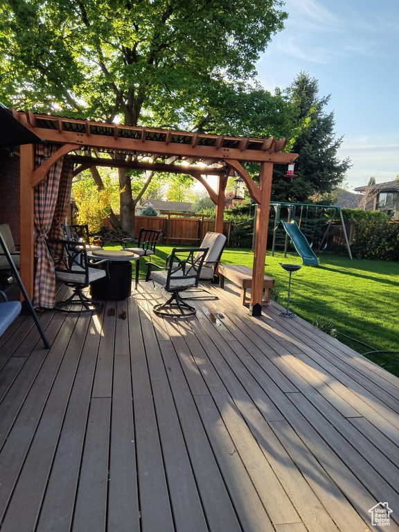 Deck featuring a playground, a pergola, and a lawn