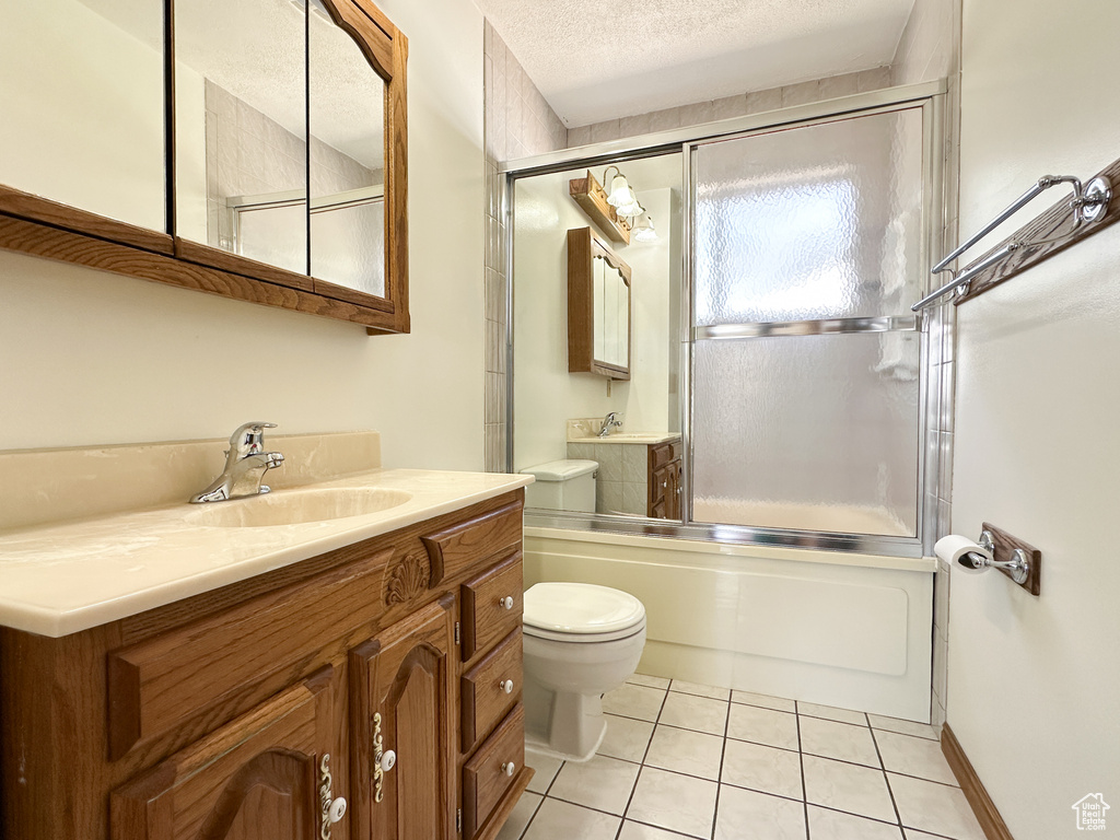 Full bathroom with large vanity, a textured ceiling, combined bath / shower with glass door, tile floors, and toilet
