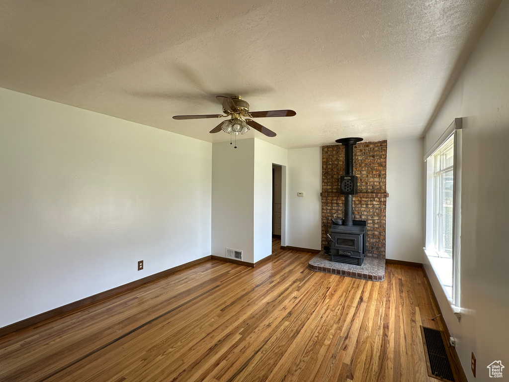 Unfurnished living room featuring a healthy amount of sunlight, hardwood / wood-style floors, a wood stove, and ceiling fan