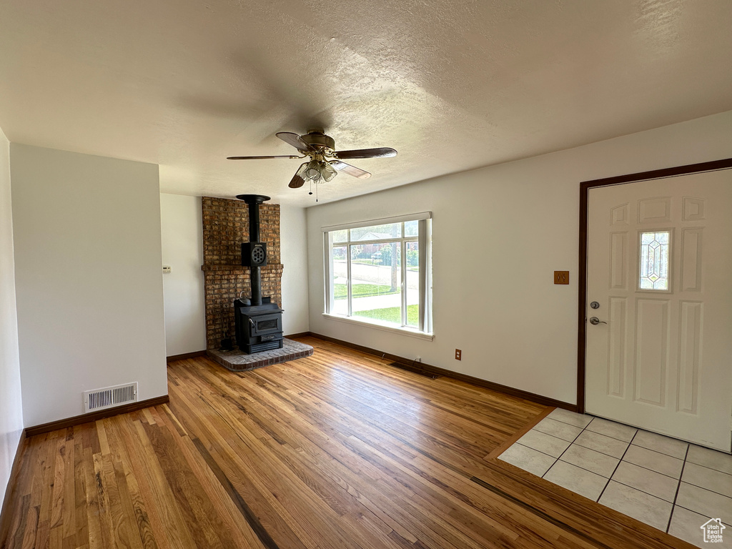 Unfurnished living room with ceiling fan, a textured ceiling, brick wall, tile floors, and a wood stove