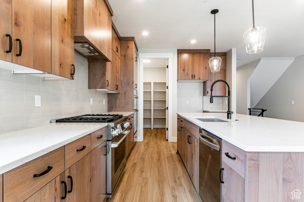 Kitchen featuring wall chimney exhaust hood, backsplash, stainless steel appliances, sink, and light hardwood / wood-style floors