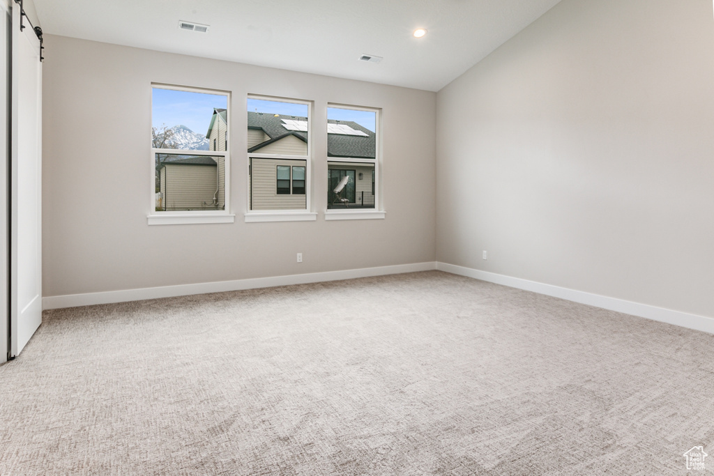 Unfurnished room with light colored carpet, plenty of natural light, and a barn door