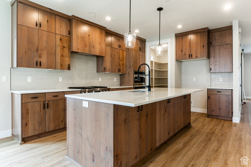 Kitchen featuring hanging light fixtures, light hardwood / wood-style floors, backsplash, and a kitchen island with sink