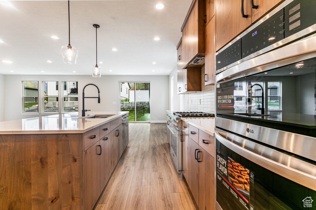 Kitchen with pendant lighting, double oven, a center island with sink, range with gas cooktop, and light hardwood / wood-style floors