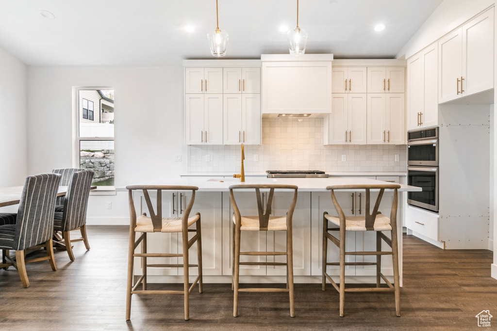 Kitchen featuring backsplash, white cabinetry, dark hardwood / wood-style flooring, stainless steel double oven, and a kitchen island with sink